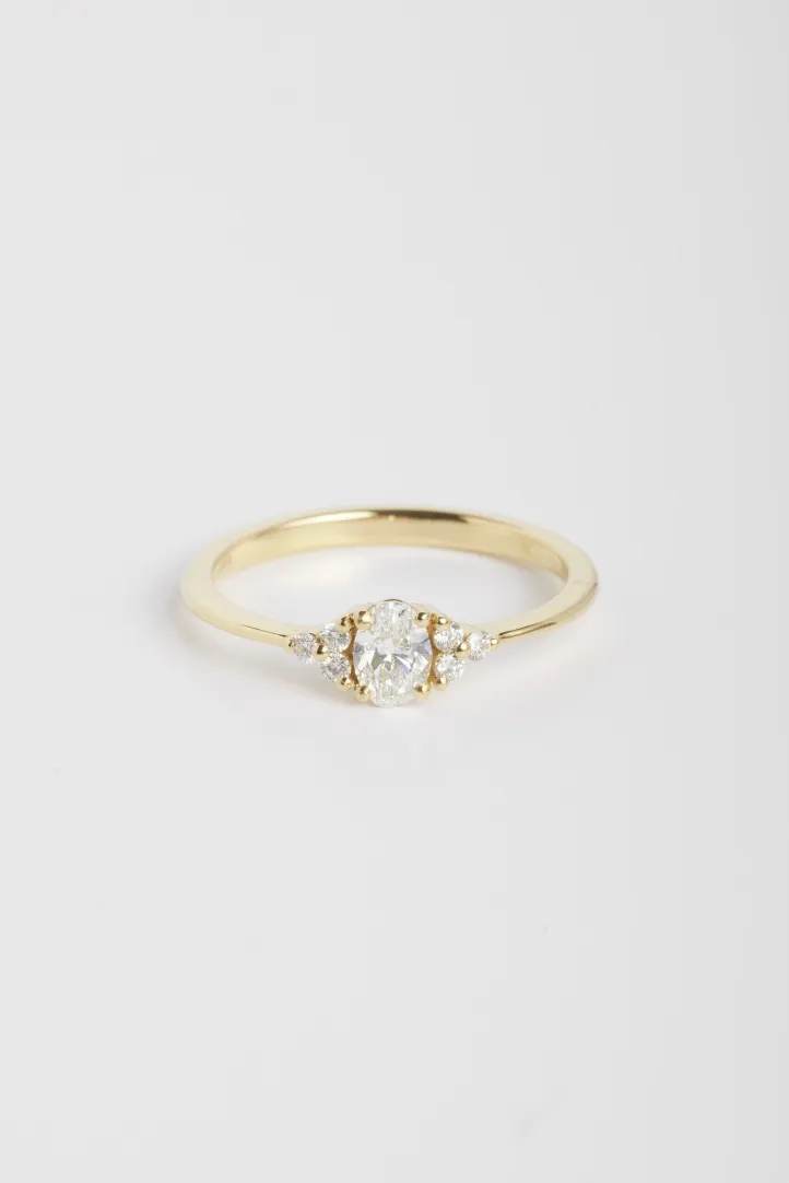 The Clara M ring, in 18k yellow gold set with an oval central diamond and accompanied by brilliant-cut diamonds. The Clara M ring, in 18k yellow gold set with an oval central diamond and accompanied by brilliant-cut diamonds.
