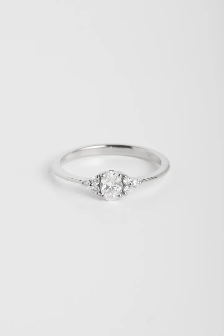 La bague Clara M, en or blanc 750‰ sertie d'un diamant central taille ovale et accompagné de diamants taille brillant. La bague Clara M, en or blanc 750‰ sertie d'un diamant central taille ovale et accompagné de diamants taille brillant.