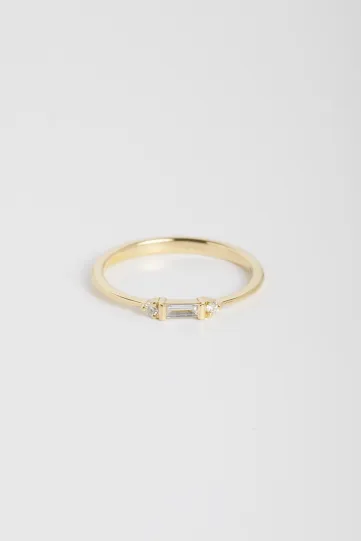 La bague Nessa, en or jaune 750‰, sertie d'un diamant taille baguette et accompagné de diamants taille brillant.