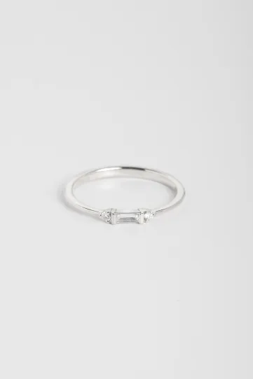 La bague Nessa, en or blanc 750‰, sertie d'un diamant taille baguette et accompagné de diamants taille brillant.